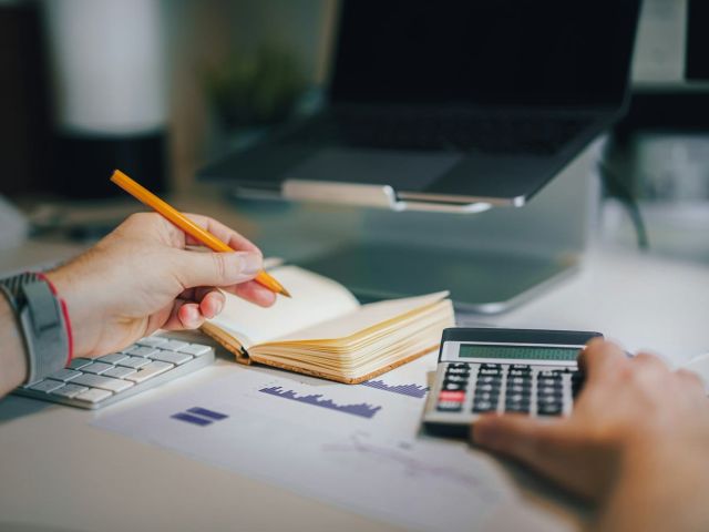 Reviewing business accounts Business owner working through figures with a notebook, calculator and laptop